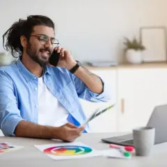 Mann im Homeoffice telefoniert, hält Farbfächer und nutzt Unified Communications as a Service für effiziente Kommunikation.
