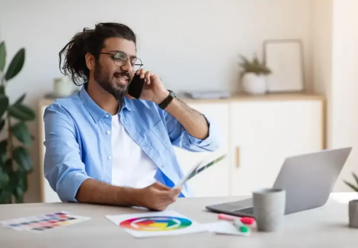 Mann im Homeoffice telefoniert, hält Farbfächer und nutzt Unified Communications as a Service für effiziente Kommunikation.