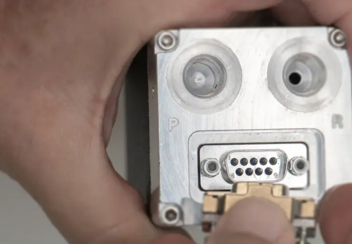 Nahaufnahme eines metallischen Geräts mit einem D-Sub-Anschluss, an den ein Stecker angeschlossen wird.