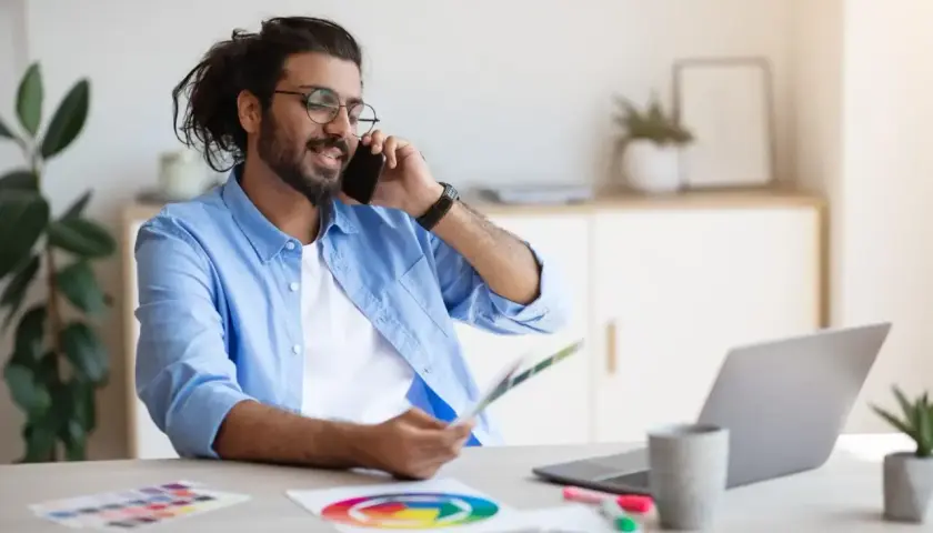 Mann im Homeoffice telefoniert, hält Farbfächer und nutzt Unified Communications as a Service für effiziente Kommunikation.