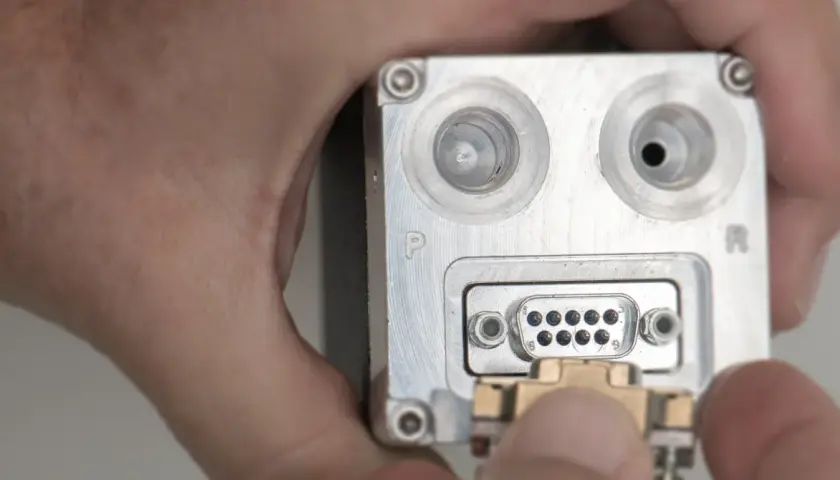 Nahaufnahme eines metallischen Geräts mit einem D-Sub-Anschluss, an den ein Stecker angeschlossen wird.