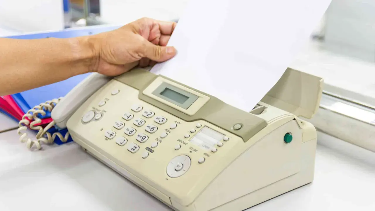 Hand führt ein Blatt Papier in ein Faxgerät ein, um ein Fax zu versenden.