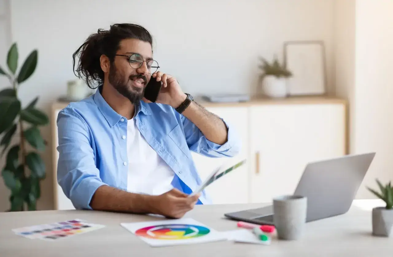 Mann im Homeoffice telefoniert, hält Farbfächer und nutzt Unified Communications as a Service für effiziente Kommunikation.