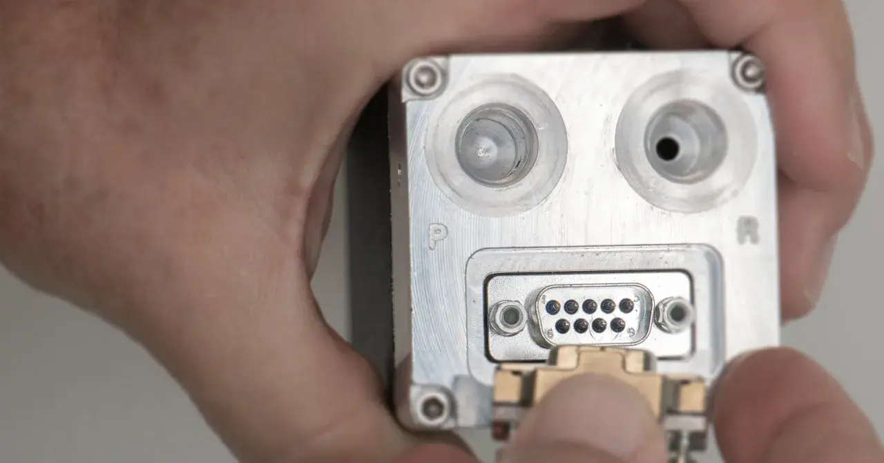 Nahaufnahme eines metallischen Geräts mit einem D-Sub-Anschluss, an den ein Stecker angeschlossen wird.