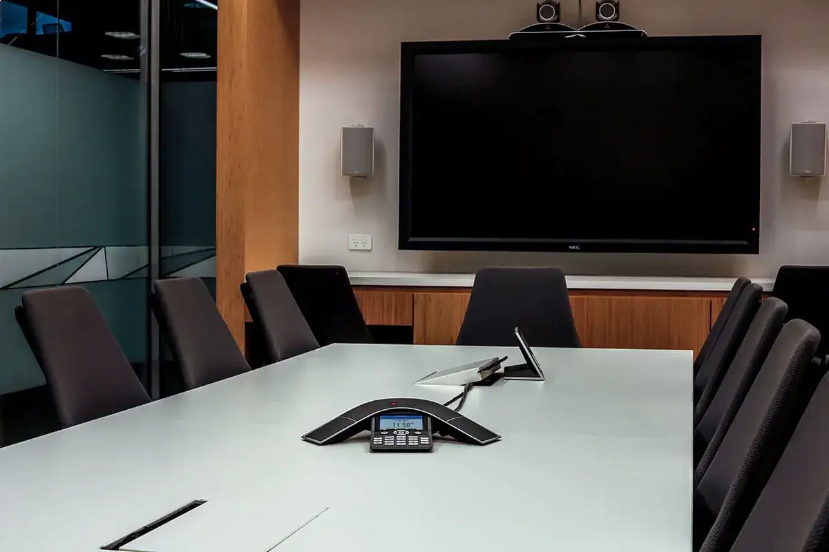 Konferenzraum mit großem Bildschirm, Lautsprechern und einem Tischtelefon für eine audio conference.